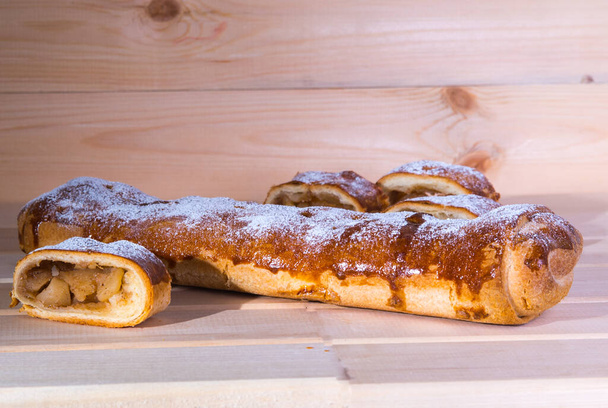  Sliced apple strudel and whole roll on wooden table, close up, view from the front - Photo, Image