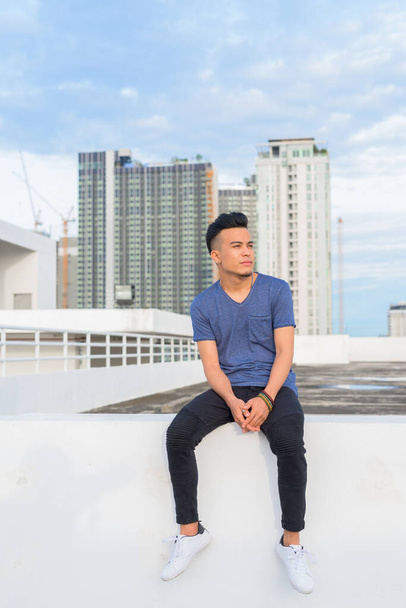 Portrait of young handsome multi ethnic man against view of the city at rooftop of the building outdoors - 写真・画像