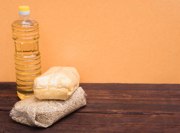 Ένα μπουκάλι ηλιέλαιο και διάφορα δημητριακά σε συσκευασία σε κίτρινο φόντο και σε ξύλινο καφέ πάγκο στην κουζίνα - Φωτογραφία, εικόνα