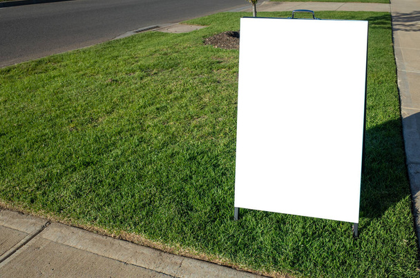 Blank white outdoor advertising stand/sandwich board mockup template. Clear street signage board placed on grass/nature stripe on side of a road. - Photo, Image