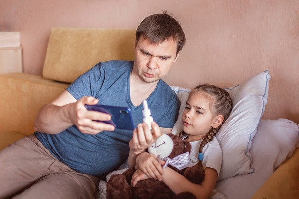 Μεσήλικας πατέρας που κοιτάζει την οθόνη του smartphone και συμβουλεύεται έναν γιατρό σε απευθείας σύνδεση στο σπίτι, υπηρεσίες τηλευγείας κατά τη διάρκεια του αποκλεισμού, μακρινή βιντεοκλήση, σύγχρονη εφαρμογή υγειονομικής περίθαλψης τεχνολογίας - Φωτογραφία, εικόνα