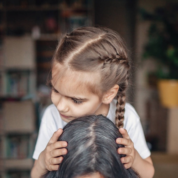 Cute little girl hugging and kissing her mature mother in the head, late motherhood, care and family support, happy mother day for all ages - Photo, Image