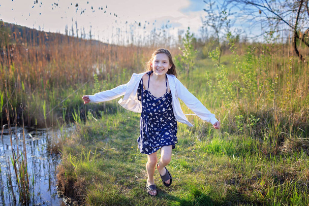 Menina bonito correndo através de um belo prado perto do lago, férias em família de verão. Diversão ao ar livre e atividade saudável, as pessoas gostam da vida após o confinamento
 - Foto, Imagem