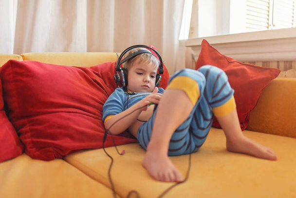 Gadget dependence, digital native generation alpha, cute kid lying on sofa and using gadgets from the early morning at home, online education and entertainment - Photo, Image