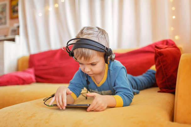 Gadget-Abhängigkeit, Digital Native Generation Alpha, niedliches Kind auf dem Sofa liegend und mit Geräten vom frühen Morgen zu Hause, Online-Bildung und Unterhaltung - Foto, Bild