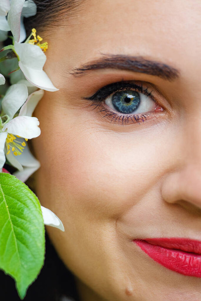 Gyönyörű fehér lány virágokkal. Egy káprázatos barna, fehér almafákkal a szeme előtt. Közelkép egy fiatal, gyönyörű nő arcáról, egészséges, tiszta bőrrel. - Fotó, kép
