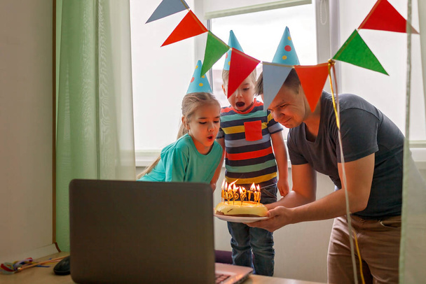 Onnellinen perhe, jossa kaksi sisarusta juhlii syntymäpäivää internetin kautta karanteeniaikana, eristäytyminen ja perhearvot, online-syntymäpäiväjuhlat, valikoiva keskittyminen kakkuun - Valokuva, kuva