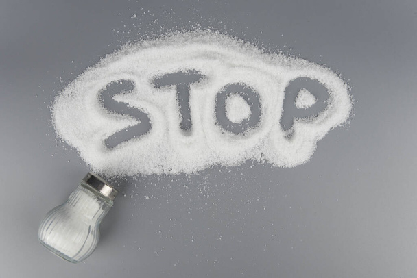 Ένας σωρός αλάτι από αλατιέρα, γράμματα με λέξη stop salt, έννοια υπερβολική πρόσληψη αλατιού και λευκό θάνατο - Φωτογραφία, εικόνα