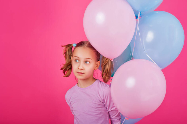 Красуня дівчина з різнокольоровими повітряними кульками сміється над рожевим тлом. Прекрасна щаслива молода жінка на святковій вечірці. Радісна модель розважається, грає і святкує з пастельною кольоровою кулею
 - Фото, зображення