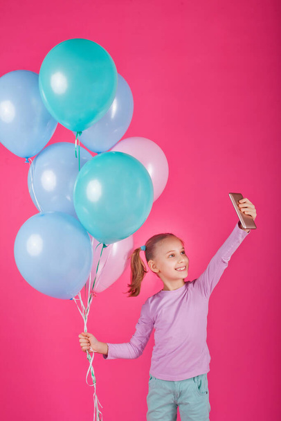 Beauty girl with colorful air balloons laughing over pink background. Beautiful Happy Young woman on birthday holiday party. Joyful model having fun, playing and celebrating with pastel color balloon - Photo, Image