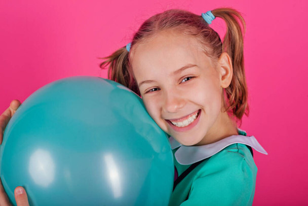 Portrait of a beautiful little girl hugging a blue balloon isolated on a pink background - Foto, immagini