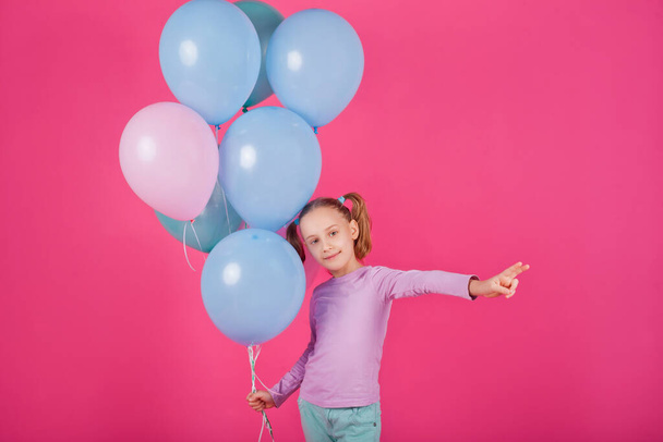 ピンクの背景を笑いながらカラフルな気球と美少女。誕生日パーティーで美しい幸せな若い女性。パステルカラーの風船で楽しさ、遊び、祝う楽しいモデル - 写真・画像