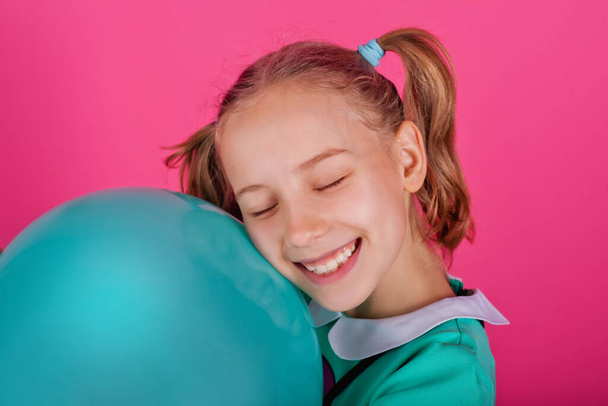 Portrait d'une belle petite fille embrassant un ballon bleu isolé sur un fond rose
 - Photo, image