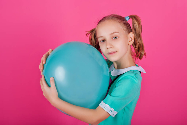 Portrait of a beautiful little girl hugging a blue balloon isolated on a pink background - Photo, Image
