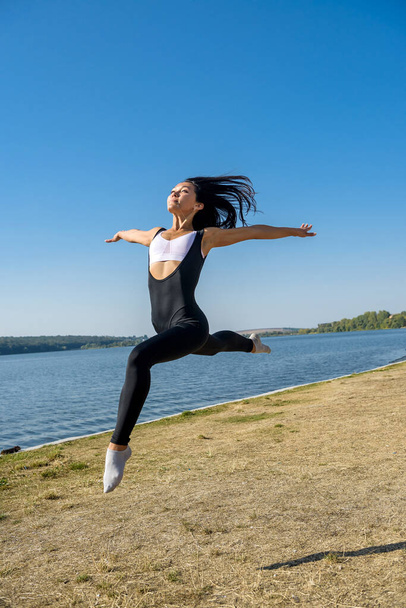 Усміхнена молода гімнастка стрибає на відкритому повітрі біля озера. Здоровий спосіб життя
. - Фото, зображення