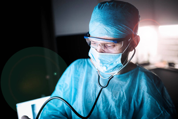 コロナウイルスパンデミック時の手術室の制服とゴーグルを着た若い男性外科医. - 写真・画像