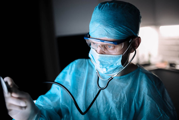 young man surgeon doctor in uniform and goggles in operating room during coronavirus pandemic. - Valokuva, kuva