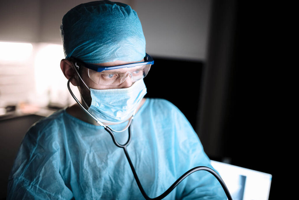 young man surgeon doctor in uniform and goggles in operating room during coronavirus pandemic. - Foto, Imagem