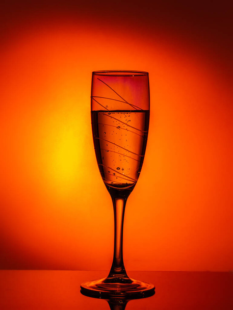A glass of champagne on an orange background with a beautiful vignette around the edge. Idea for decorating a party or holiday - Fotografie, Obrázek