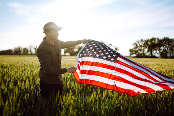 Young man proudly hold waving american USA flag. Patriot raise national american flag against the blue sky. Independence Day, 4th July - Φωτογραφία, εικόνα