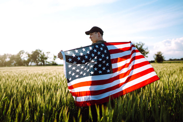 Young man proudly hold waving american USA flag. Patriot raise national american flag against the blue sky. Independence Day, 4th July - Φωτογραφία, εικόνα