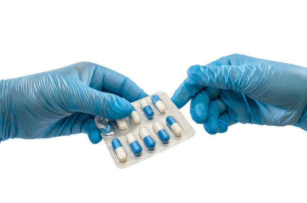 Руки в синіх рукавичках дають або приймають таблетки, ізольовані на білому тлі. Крупним планом. Медична концепція
. - Фото, зображення