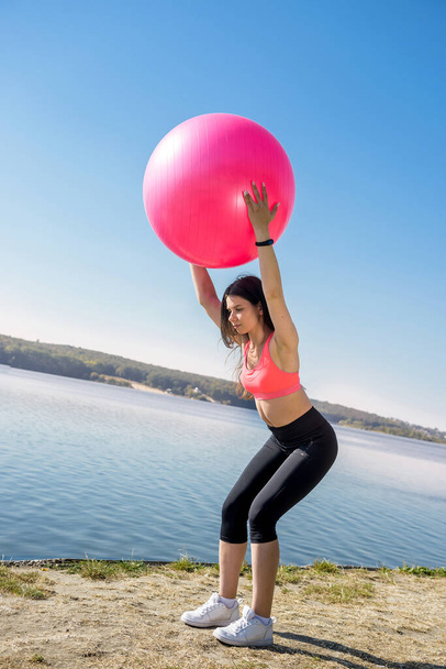 Νεαρή γυναίκα σε φόρμα στα αθλητικά κατά τη διάρκεια της γυμναστικής και την άσκηση με μπάλα στη λίμνη. Υγιής τρόπος ζωής - Φωτογραφία, εικόνα