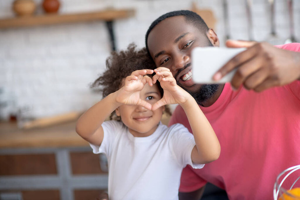Sweet little girl showing heart sign while her father making selfie - Fotografie, Obrázek