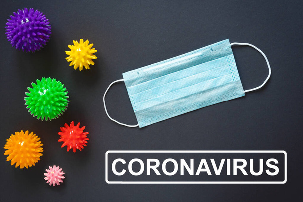 Coronavirus word on a gray background. Medical mask on the table. Covid 19 in the form of balls with needles. The concept of an epidemic. - Zdjęcie, obraz