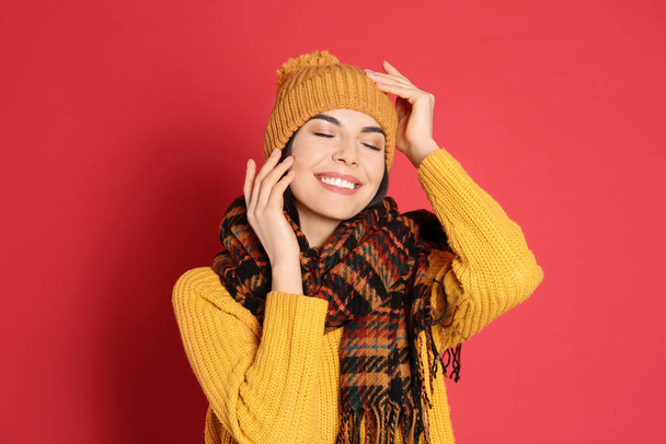 Young woman wearing warm sweater, scarf and hat on red background. Winter season - Foto, Bild