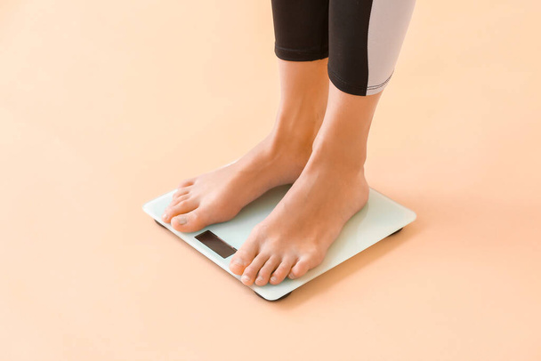 Jovem mulher medindo seu peso sobre fundo de cor
 - Foto, Imagem