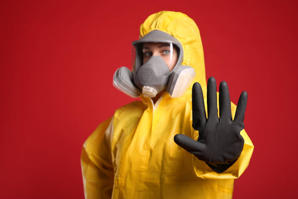 Woman in chemical protective suit making stop gesture against red background, focus on hand. Virus research - Foto, Imagen