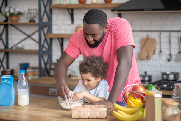African american bearded man playing with his daughter stirring the flour in the bowl - Foto, Bild