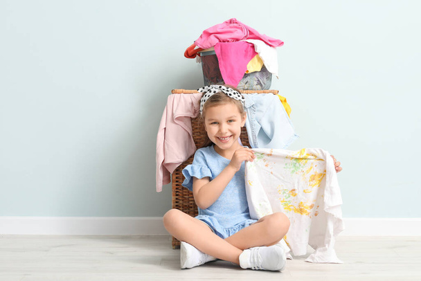 Kleines Mädchen mit schmutziger Wäsche sitzt in der Nähe einer Lichtwand - Foto, Bild