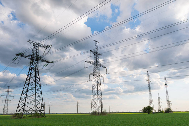 Nagyfeszültségű elektromos vezetékek vezetnek át a zöld mezőn. Villamosenergia-szállítás mezőgazdasági területeken keresztül történő támogatás révén. - Fotó, kép