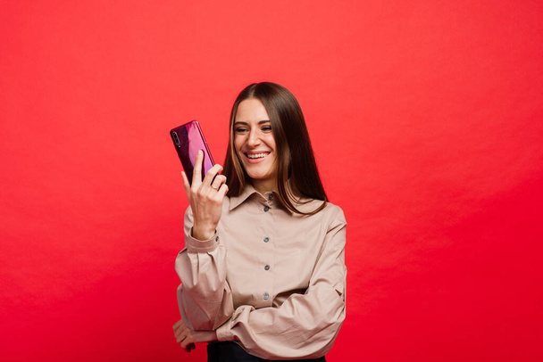 Surprised young woman using smart phone, red background - Photo, Image