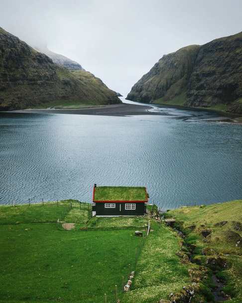 Lonely seaside house with green roof between the foggy green mountains, Faroe islands, Saksun village. Vertical nature photo. - Φωτογραφία, εικόνα