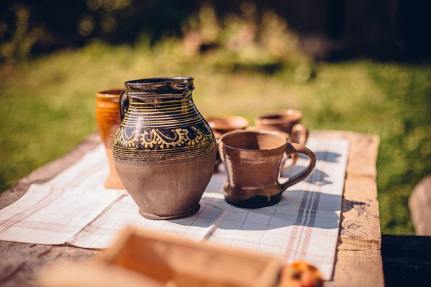 A closeup shot of clay pots and cups on an outdoor wooden table - Φωτογραφία, εικόνα