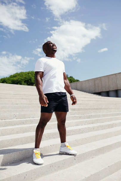 Full-length portrait of a professional athlete in a white T-shirt enjoying fresh air on the street before starting sports - Fotó, kép