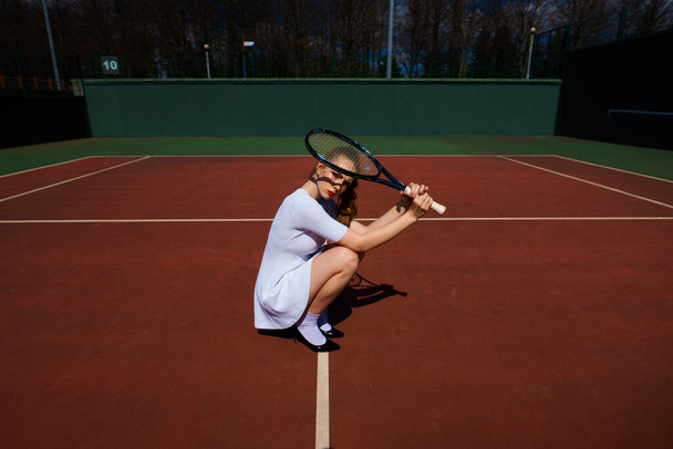 Seksikäs tyttö tennispelaaja valkoinen mekko ja korkokengät tilalla tennismaila kentällä. Nuori nainen pelaa tennistä, urheilu - Valokuva, kuva