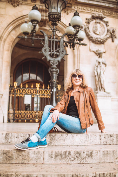Woman tourist in jeans and a leather jacket is resting and enjoying the view on the steps of an old building - Foto, Bild