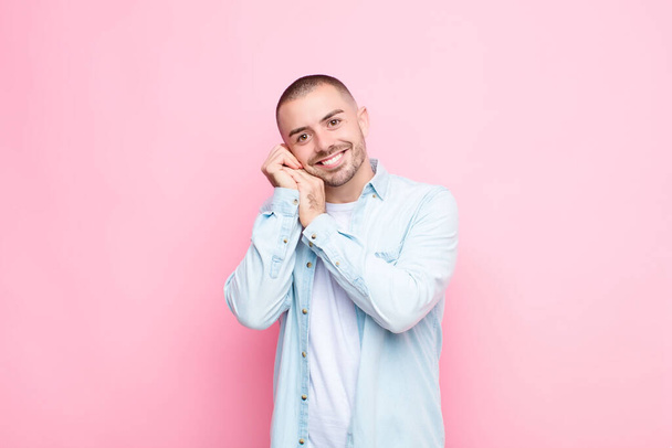 young handsome man feeling in love and looking cute, adorable and happy, smiling romantically with hands next to face against flat wall - Foto, imagen