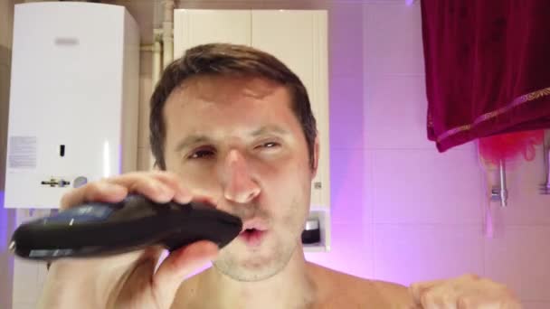 Een man in de badkamer scheert, zingt en danst tegelijkertijd - Video