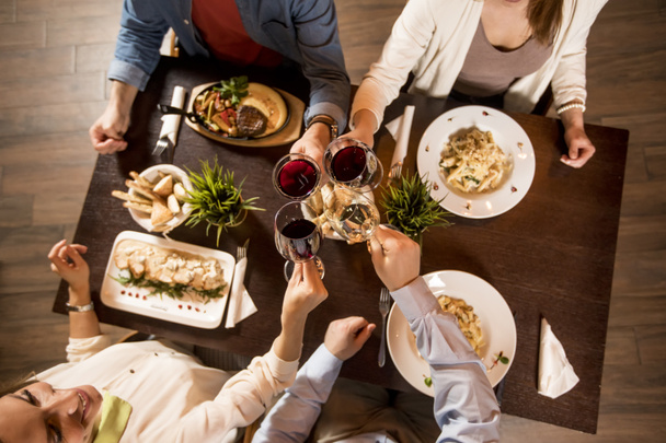 Čtyři ruce s červeným vínem toasting přes servírovaný stůl s jídlem v restauraci - Fotografie, Obrázek