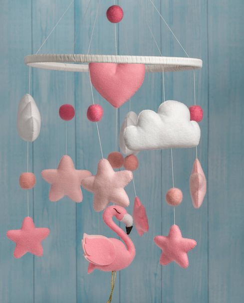 Colorful and eco-friendly children's mobile from felt for children. It consists of flamingo toys, clouds, stars and balloons. Handmade on blue background made from wood. - Photo, Image