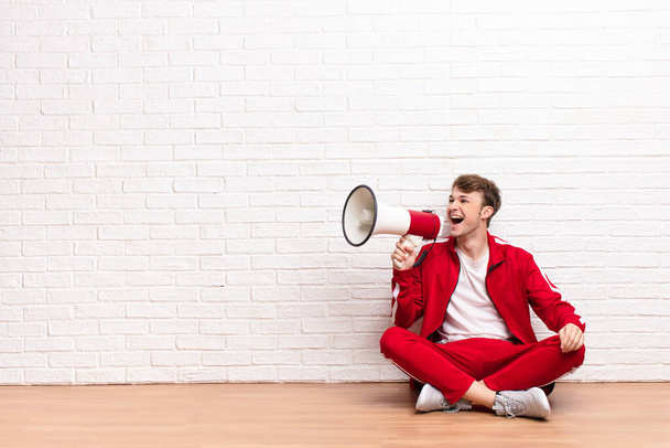 young blonde man sitting on the floor with a megaphone - Foto, imagen