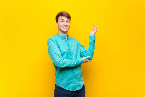 young blonde man smiling proudly and confidently, feeling happy and satisfied and showing a concept on copy space isolated against flat wall - Foto, afbeelding