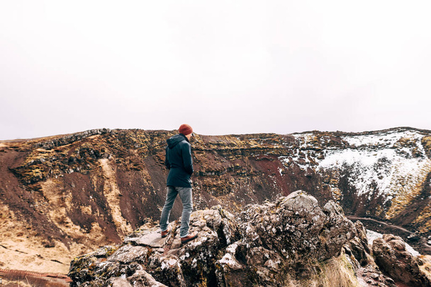 Facet stoi na skale nad jeziorem Kerid - kraterowym jeziorem wulkanicznym na Islandii. Czerwona gleba wulkaniczna, podobna do marsjańskich krajobrazów. Lubi widok z góry.. - Zdjęcie, obraz