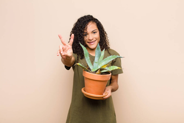 young black woman smiling and looking happy, carefree and positive, gesturing victory or peace with one hand holding a cactus - Foto, immagini
