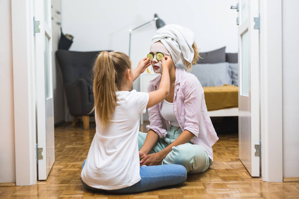 daughter helping her mother to apply cosmetic face mask at home - Foto, Imagem